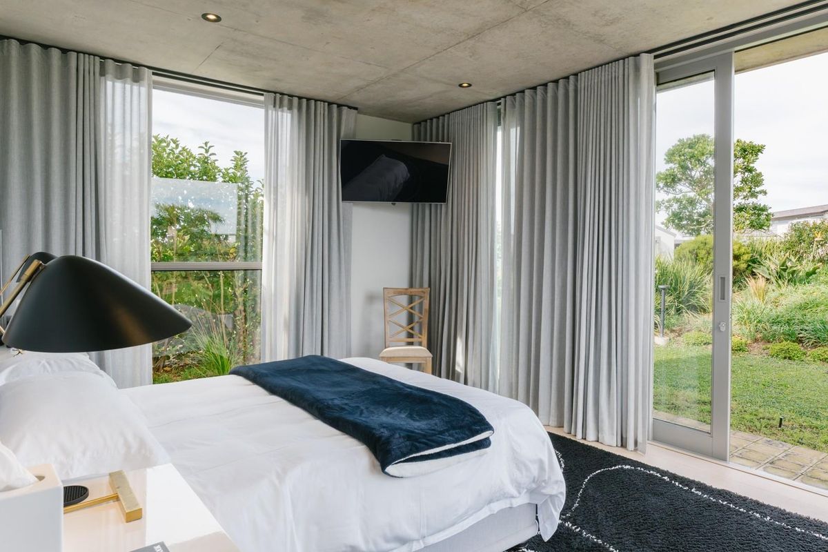 Modern bedroom featuring an exposed concrete ceiling, recessed lighting, and floor-to-ceiling glass doors providing seamless access to the garden.