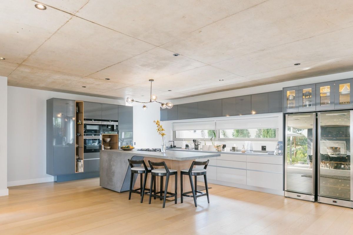 Modern open-plan kitchen featuring a concrete ceiling, sleek grey cabinetry, a central island with seating, and integrated high-end appliances.