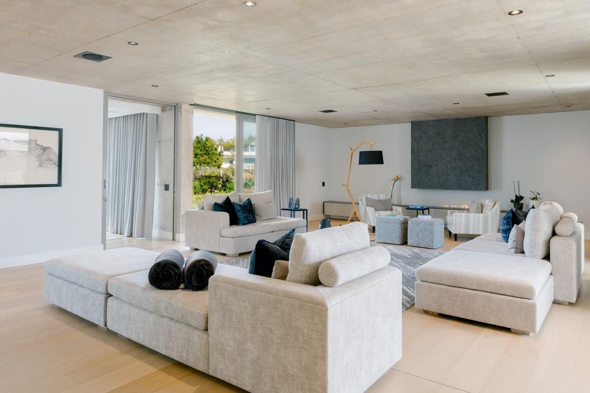 Spacious modern living room featuring an exposed concrete ceiling, hardwood flooring, and a sleek built-in fireplace with seamless access to the outdoor area.