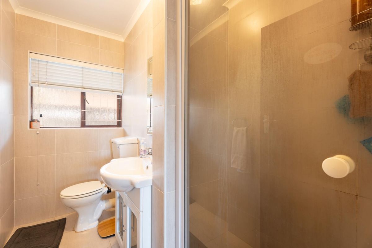 A clean, well-maintained bathroom featuring neutral wall tiles, a modern vanity with basin, a toilet, and a glass-enclosed shower.