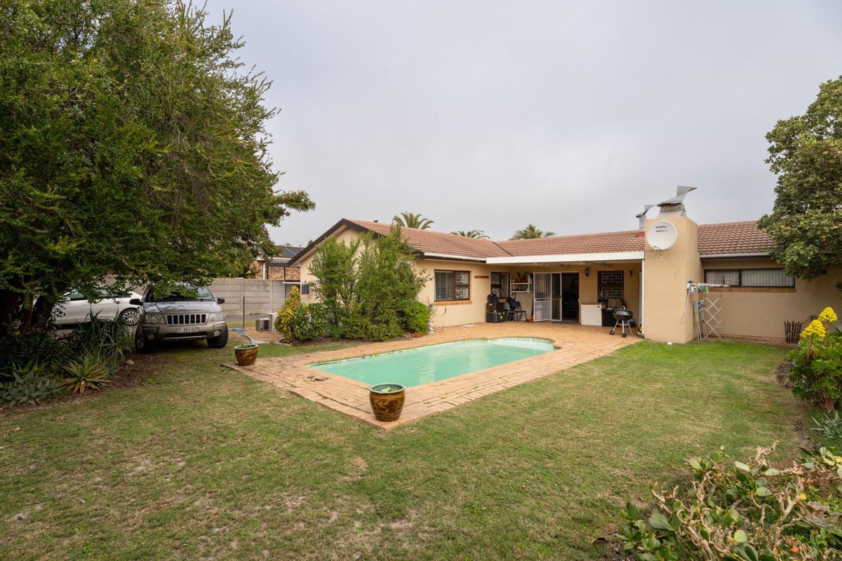 Rear exterior view of the house featuring a swimming pool, brick paved surround, and a covered patio area set within a private garden.