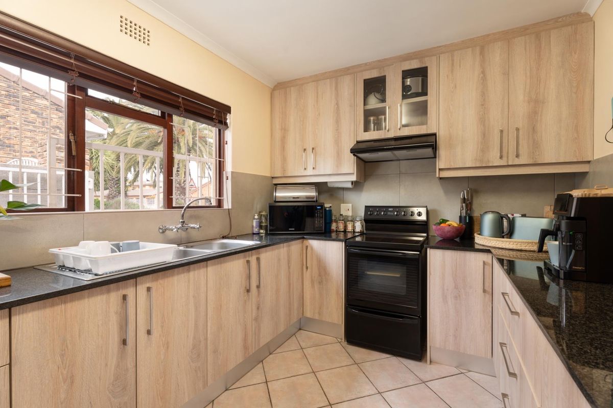 A functional kitchen featuring light wood-look cabinetry, dark granite countertops, a double basin sink, and a freestanding oven with an integrated extractor fan.