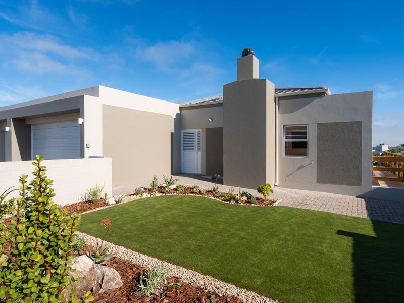 Modern single-story house exterior featuring a clean facade, integrated garage, chimney, and a well-maintained front garden with artificial turf and paved pathways.