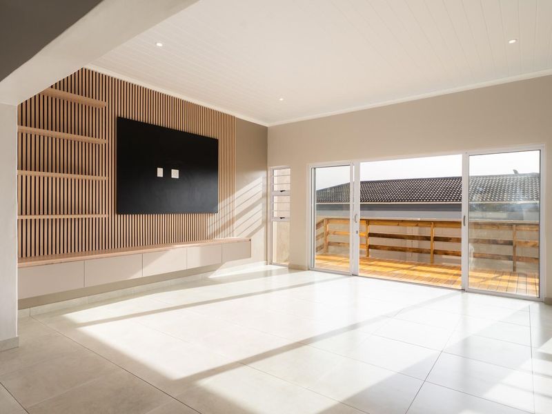 Bright and modern living area featuring a stylish slatted timber feature wall, built-in cabinetry, tiled floors, and large sliding doors opening onto a timber deck.