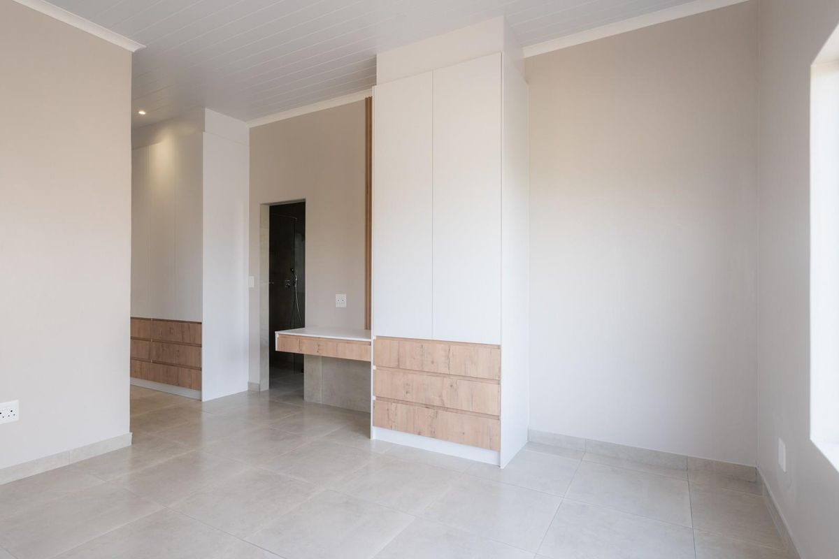 A bright, modern bedroom featuring neutral tones, built-in cabinetry with integrated desk space, and large windows providing ample natural light.