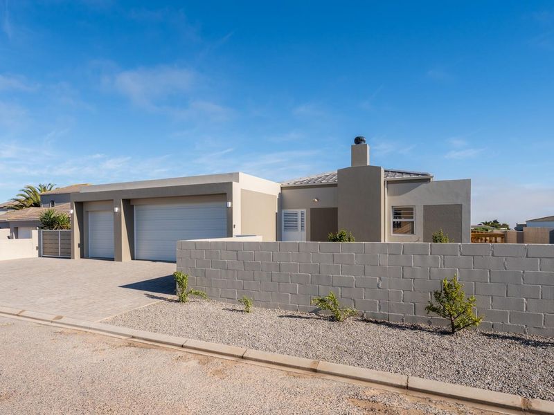 Modern single-story house featuring a double garage, paved driveway, and a concrete block boundary wall under a clear blue sky.