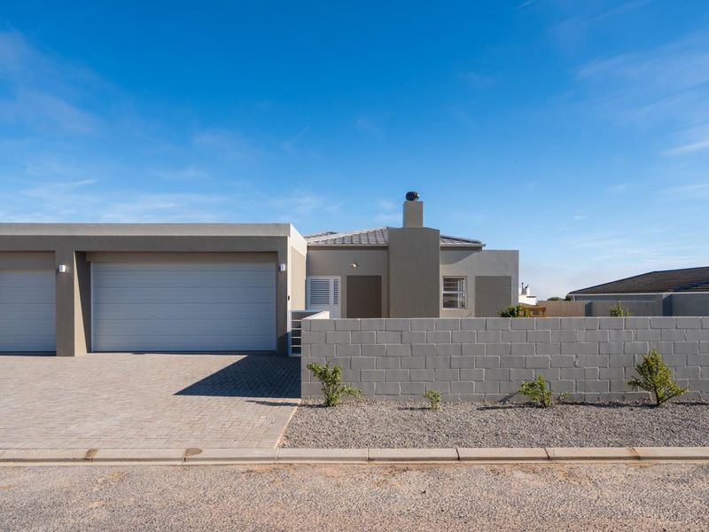 Modern single-story residence featuring a double garage, paved driveway, and a clean, minimalist facade with a prominent chimney.