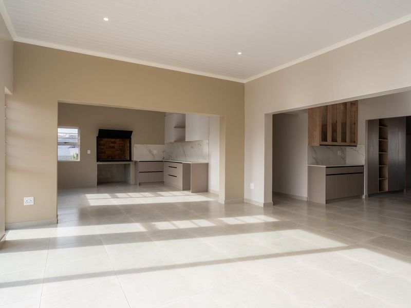 Spacious open-plan living area featuring a modern kitchen with stone countertops and a built-in braai, leading out to a patio through sliding glass doors.