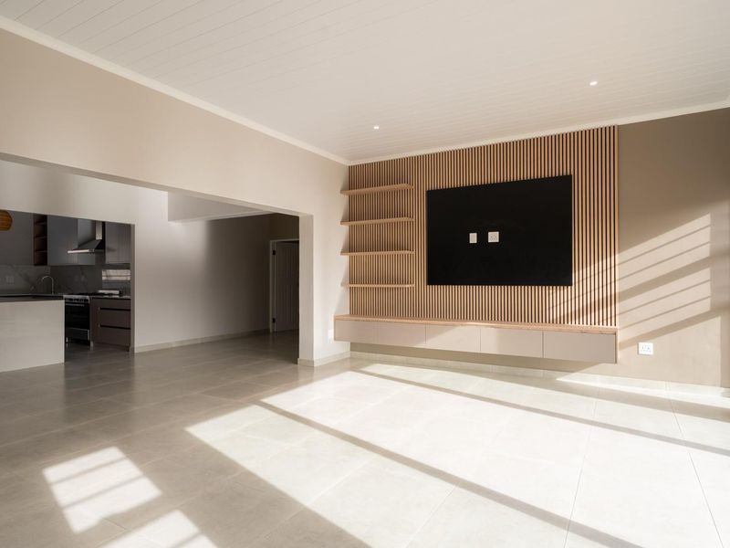 Spacious open-plan living area featuring a modern slatted timber feature wall with built-in cabinetry, flowing seamlessly into a contemporary kitchen with an island.