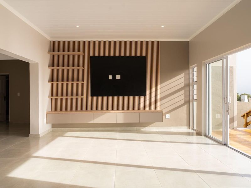 Spacious living area featuring a modern slatted timber feature wall with built-in floating cabinetry, tiled floors, and large sliding doors opening to a timber deck.
