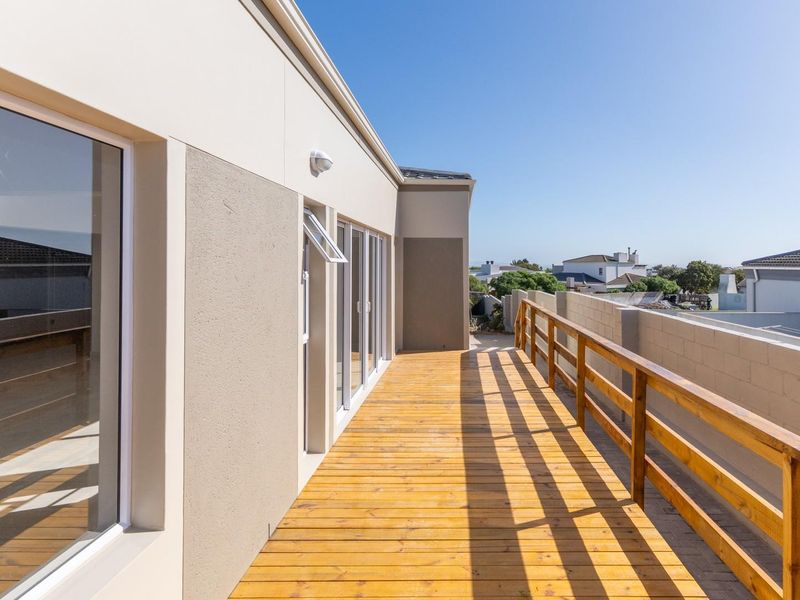 A spacious elevated timber balcony featuring a wooden balustrade, sliding glass door access, and views of the surrounding residential neighborhood.
