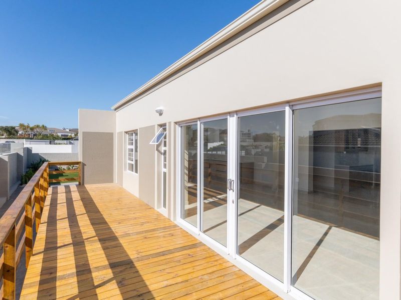 Spacious elevated timber balcony featuring a wooden balustrade and large sliding glass doors providing seamless access to the interior living space.
