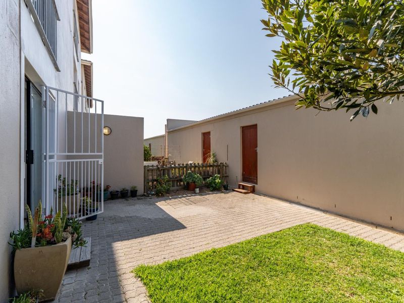 A private rear courtyard featuring paved flooring, a small lawn area, and secure access points to the apartment.
