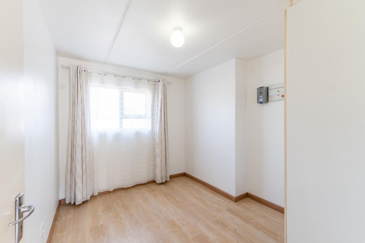 A bright, empty bedroom featuring light-toned laminate flooring, neutral walls, and a wall-mounted electrical distribution board.