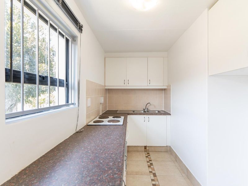 A compact, functional kitchen featuring white cabinetry, a dark laminate countertop, an electric hob, and a stainless steel sink with tiled backsplash.