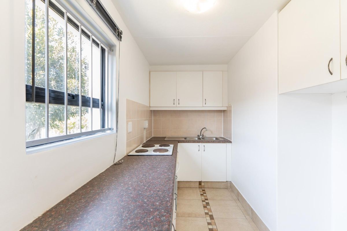 A compact, functional kitchen featuring white cabinetry, a dark laminate countertop, an electric hob, and a stainless steel sink with tiled backsplash.