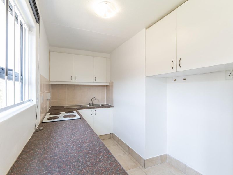 A compact, functional kitchen featuring white cabinetry, laminate countertops, an electric hob, and tiled splashbacks, offering a clean and practical workspace.