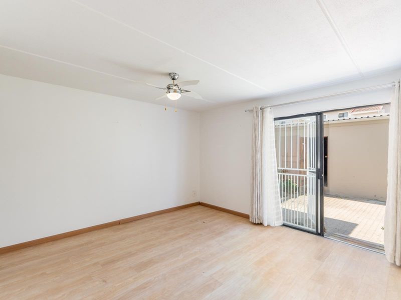 Bright and spacious living area featuring light laminate flooring, a ceiling fan, and a sliding glass door providing access to the exterior.