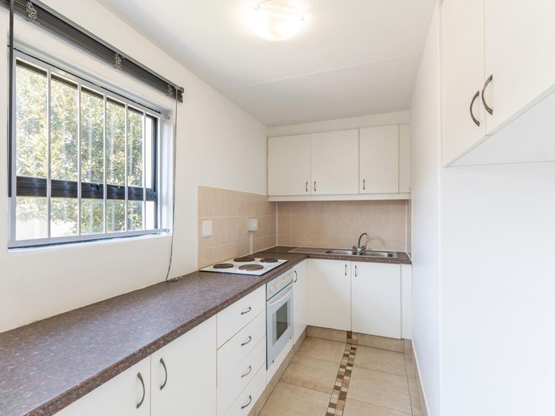 A compact, functional kitchen featuring white cabinetry, laminate countertops, an electric hob, built-in oven, and tiled flooring.