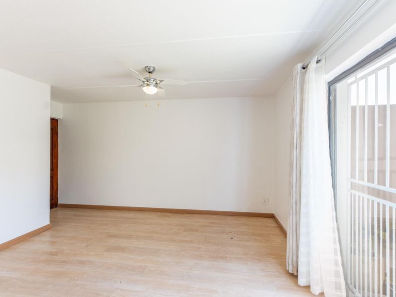 A bright, empty living room featuring light-toned laminate flooring, a ceiling fan, and a sliding glass door with an integrated security gate.