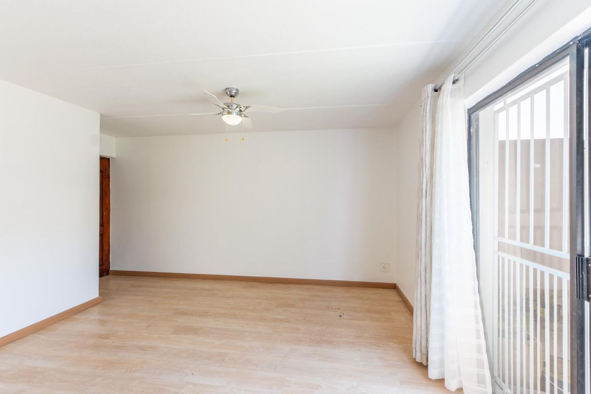 A bright, empty living room featuring light-toned laminate flooring, a ceiling fan, and a sliding glass door with an integrated security gate.