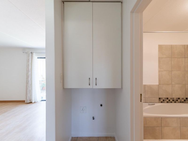 A dedicated laundry nook featuring built-in overhead cabinetry and essential plumbing and electrical connections, conveniently located adjacent to the bathroom.