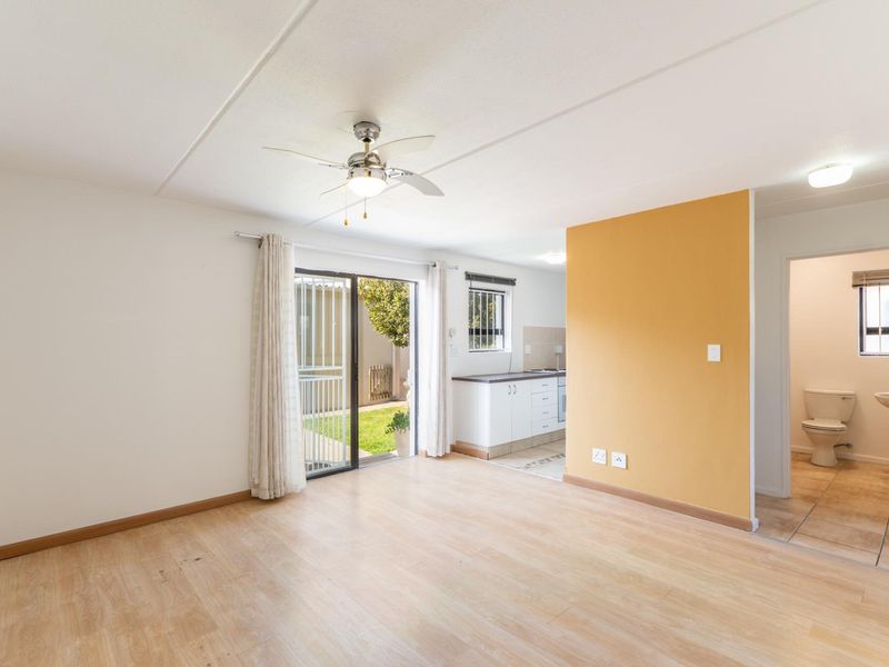 An open-plan living area featuring laminate flooring, a ceiling fan, and direct access to a private garden, with an adjacent kitchen and bathroom.