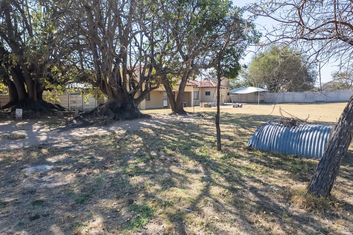 Spacious rear garden area featuring mature trees, a precast concrete boundary wall, and a covered patio attached to the main dwelling.