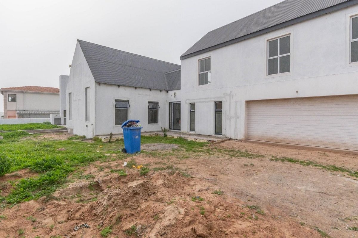 Rear view of a two-story residential property featuring a double garage, plastered exterior walls, and an unfinished garden area.