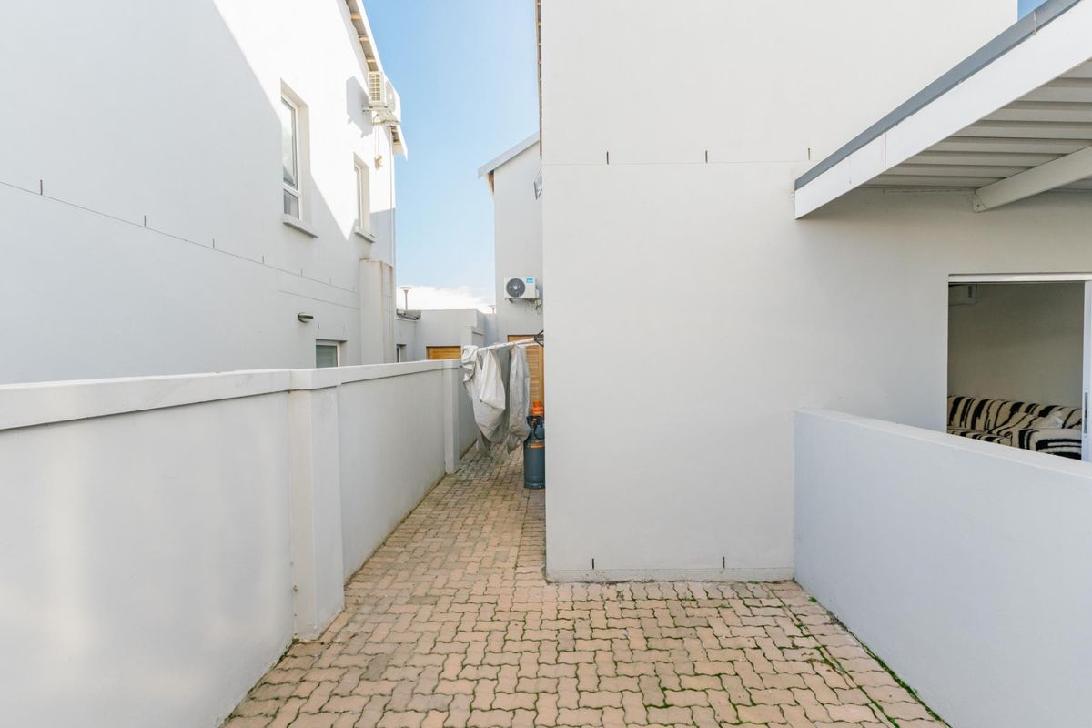 A paved side walkway or rear courtyard area between townhouse structures, featuring boundary walls and an external air conditioning unit.