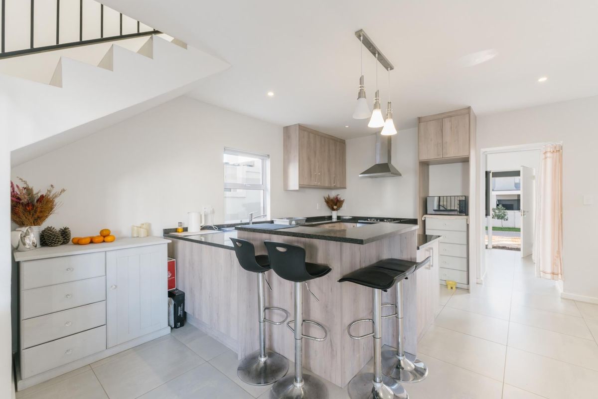 Modern kitchen featuring light wood-grain cabinetry, granite countertops, a breakfast bar, and tiled flooring, situated beneath an open staircase.