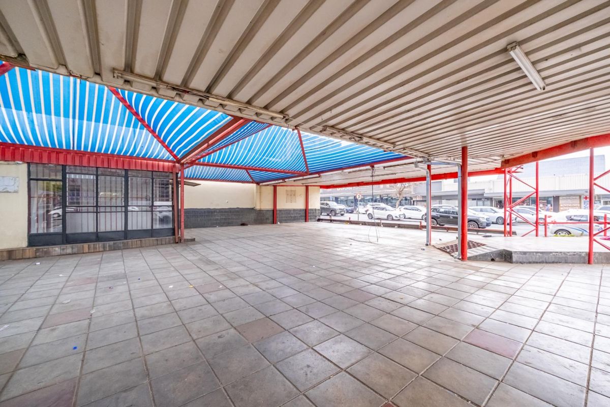A large, covered outdoor retail space featuring tiled flooring, a metal canopy structure, and a glass storefront entrance.