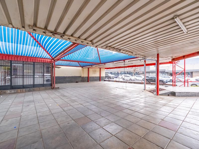 A large, covered outdoor retail space featuring tiled flooring, a metal canopy structure, and a glass storefront entrance.