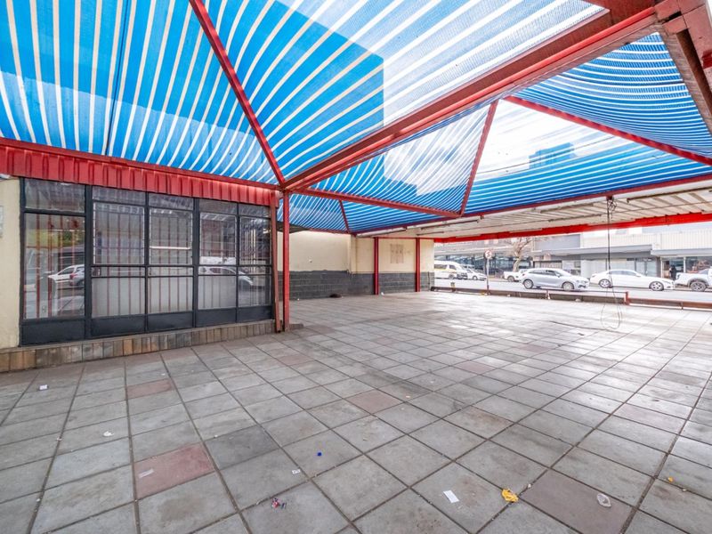 A covered outdoor retail patio area featuring tiled flooring, a metal structural frame, and a striped canopy, suitable for outdoor display or customer seating.