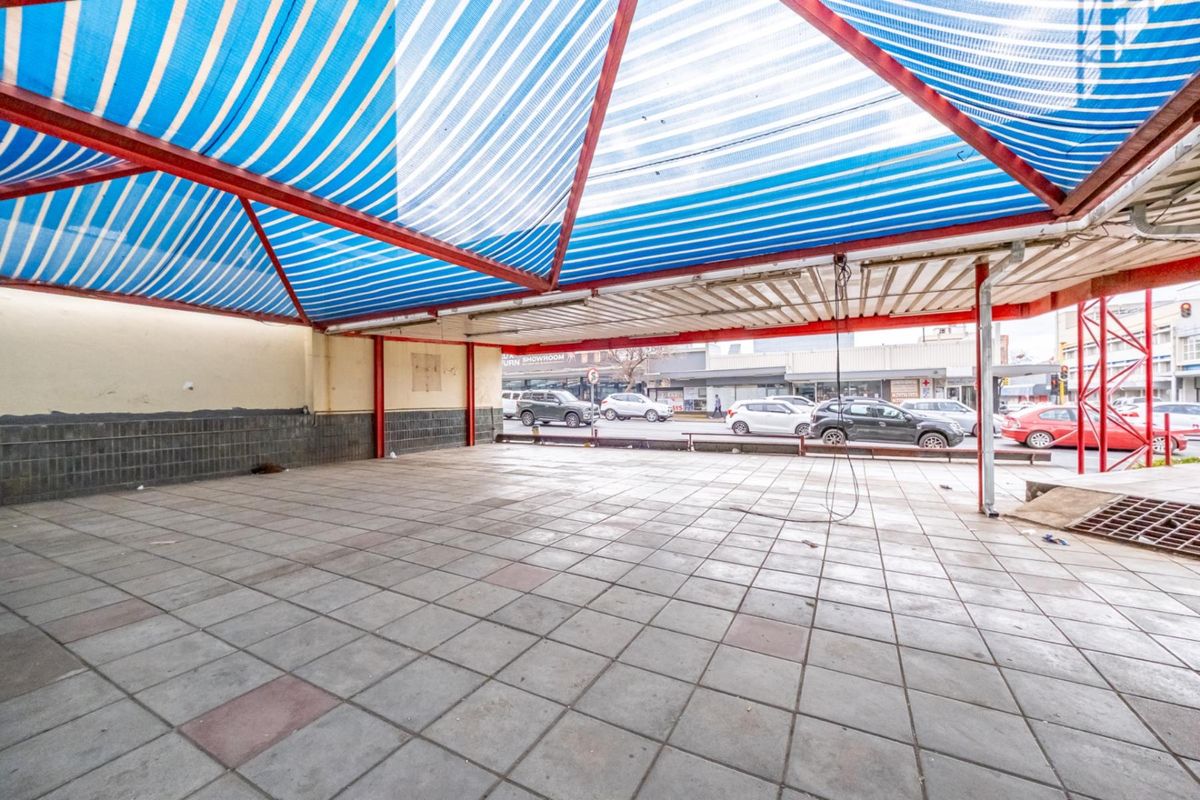 An open-plan outdoor retail or display area featuring tiled flooring and a large striped canopy structure, providing covered street-facing space.