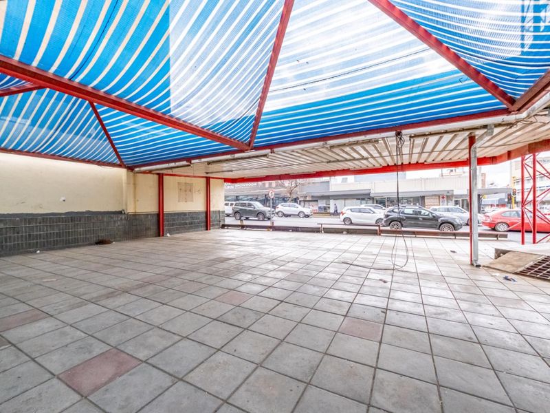 An open-plan outdoor retail or display area featuring tiled flooring and a large striped canopy structure, providing covered street-facing space.