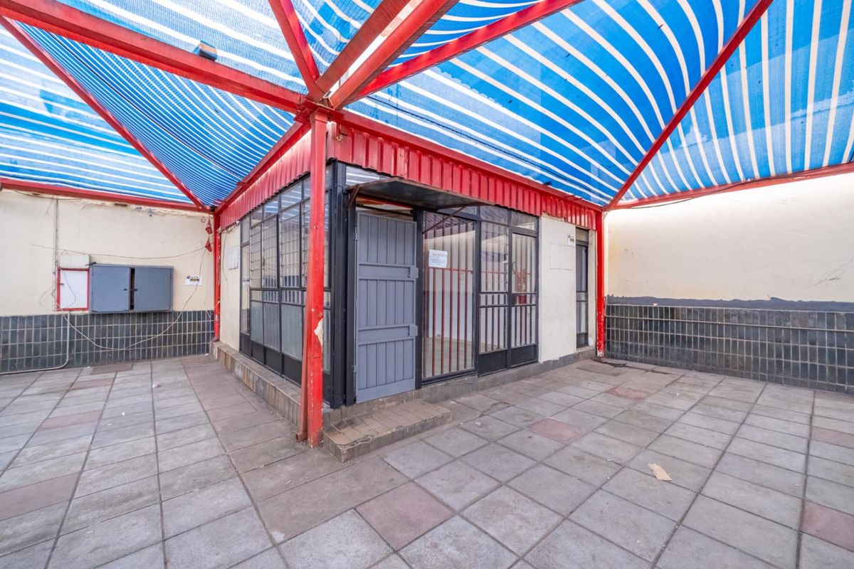 Exterior rear area featuring a covered patio with a metal frame structure, striped canopy, and tiled flooring, suitable for outdoor retail or utility use.