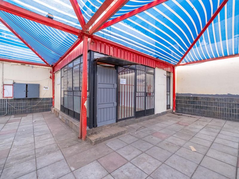 Exterior rear area featuring a covered patio with a metal frame structure, striped canopy, and tiled flooring, suitable for outdoor retail or utility use.