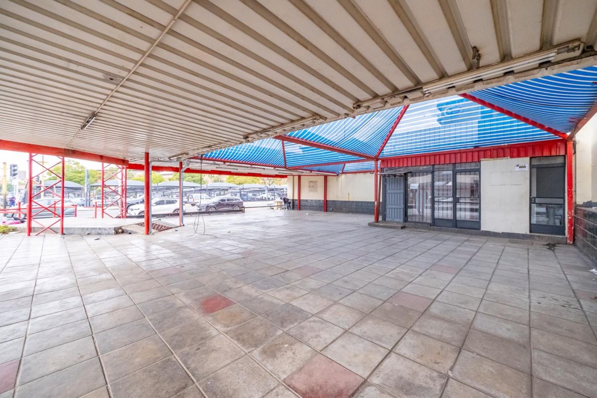 A large covered outdoor retail patio area featuring tiled flooring, metal structural supports, and a protective roof canopy.