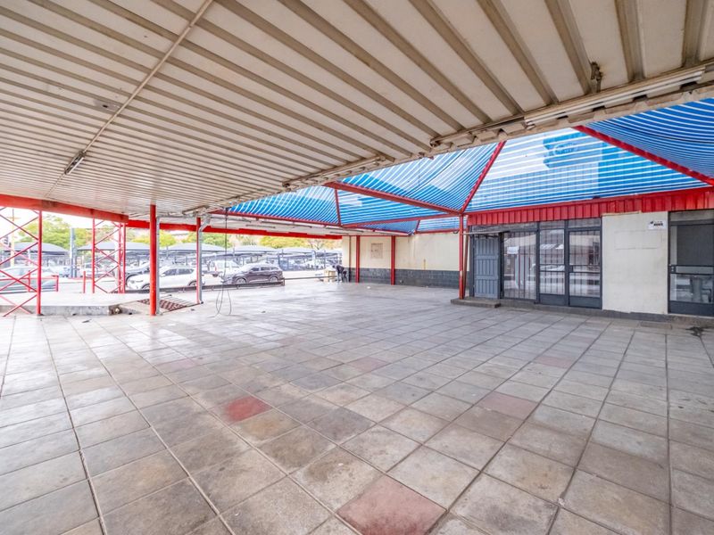 A large covered outdoor retail patio area featuring tiled flooring, metal structural supports, and a protective roof canopy.