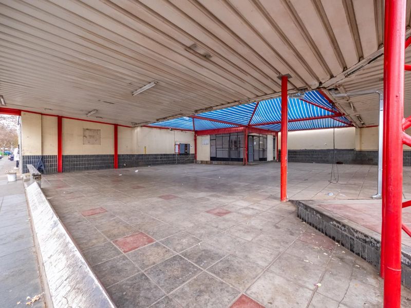 A large, covered outdoor retail patio area featuring tiled flooring, metal support columns, and a striped awning, suitable for various commercial uses.