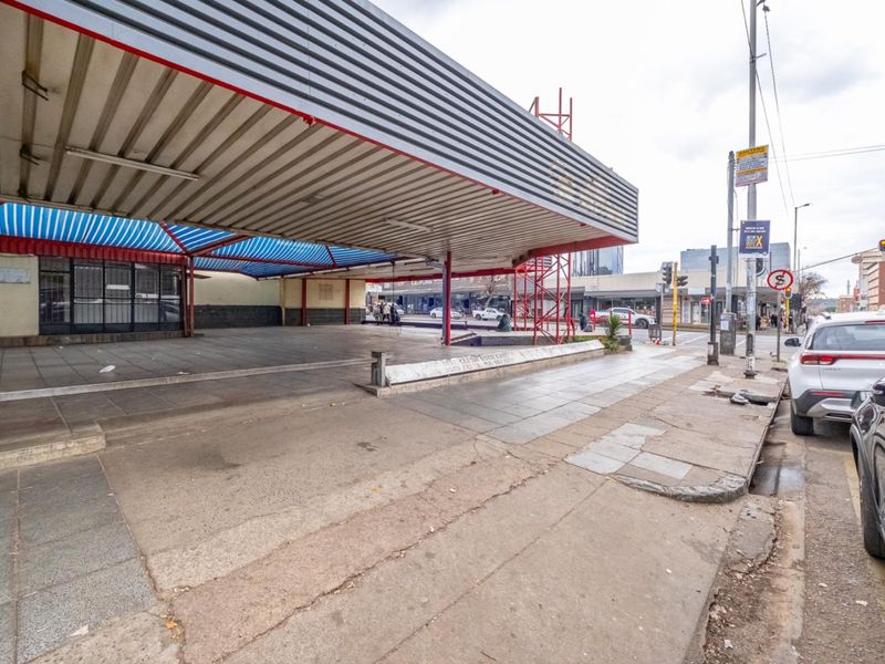 Street-level view of a retail property featuring a large metal canopy, paved forecourt area, and direct access to the main road.