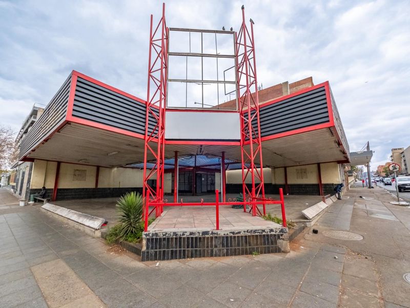 Street-level view of a commercial retail property featuring a prominent metal signage frame and a covered entrance area with tiled facade detailing.
