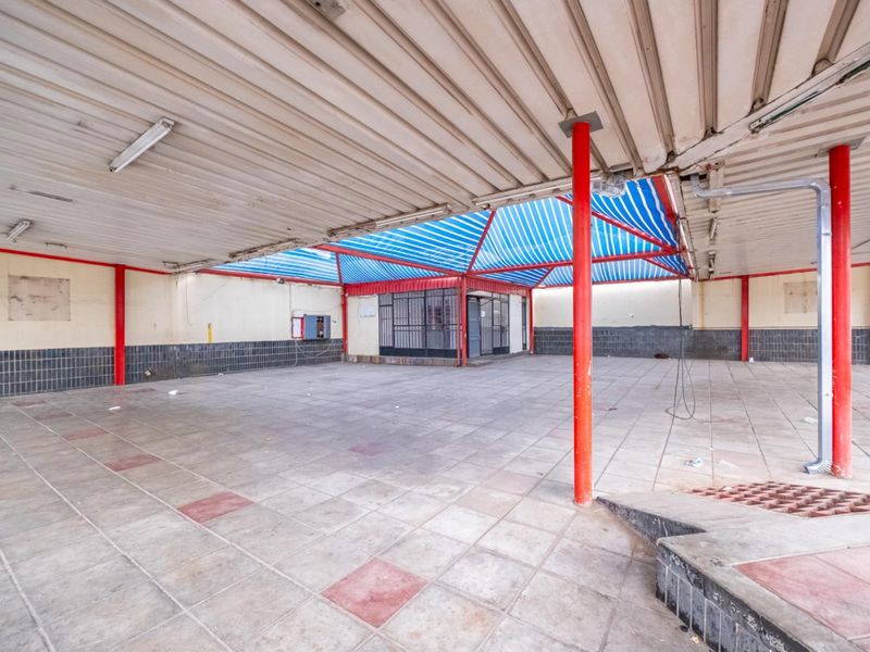 A large, covered outdoor retail or commercial space featuring tiled flooring, metal support columns, and a retractable awning structure.