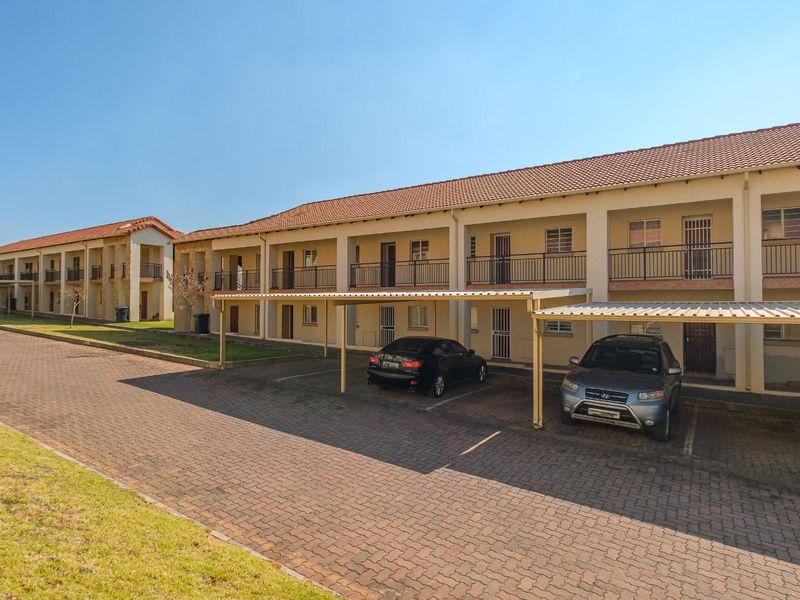 Exterior view of a multi-story apartment complex featuring covered parking bays, paved driveway, and balcony access for upper-level units.