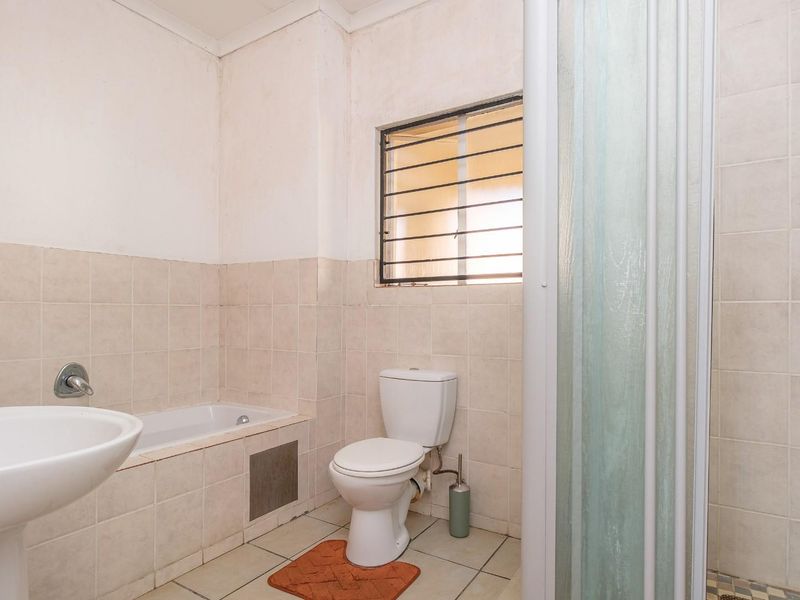 A functional bathroom featuring a pedestal basin, built-in bathtub, toilet, and a separate shower enclosure with tiled finishes throughout.