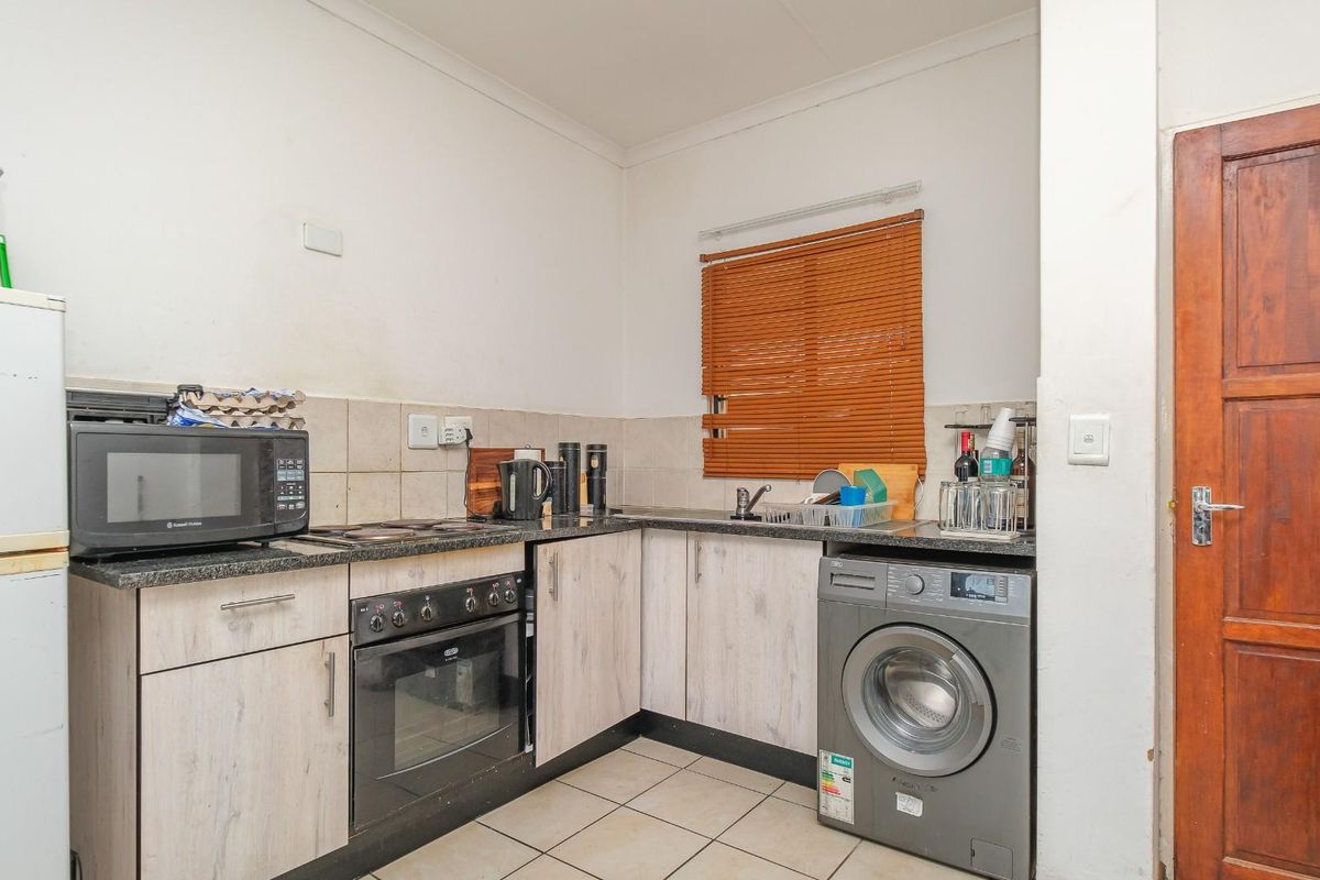 Compact kitchen featuring light wood-finish cabinetry, granite countertops, built-in oven and hob, and tiled flooring with space for a washing machine.