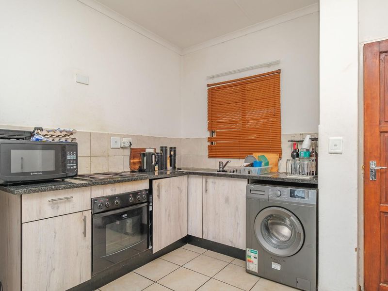 Compact kitchen featuring light wood-finish cabinetry, granite countertops, built-in oven and hob, and tiled flooring with space for a washing machine.