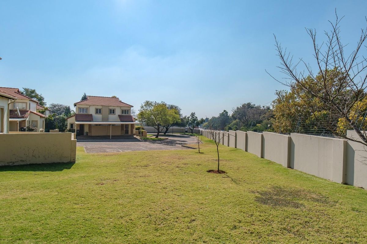 A view of the rear communal garden area featuring a well-maintained lawn, perimeter wall with electric fencing, and paved driveway access to the apartment units.