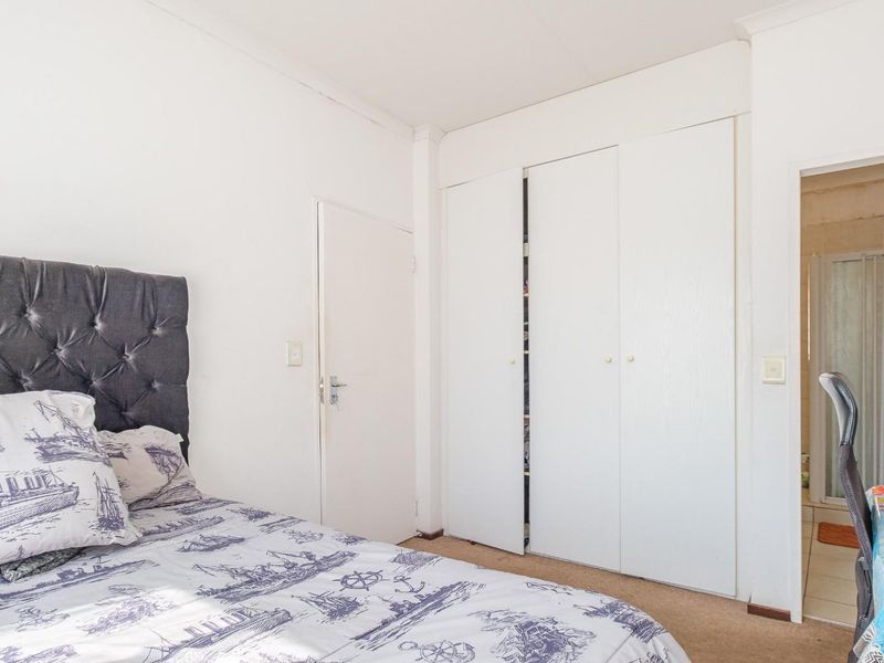 A bedroom featuring built-in cupboards and direct access to an en-suite bathroom, with neutral walls and carpeted flooring.